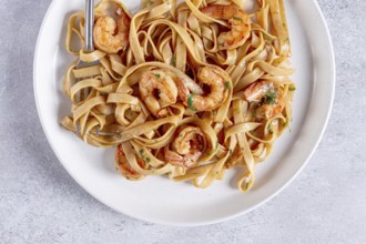 Fettuccine pasta with shrimp, spicy in soy sauce, on a grey plate with a fork, close-up