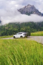 A car on a path with towering mountains in the background and damp fog, electric car on holiday,