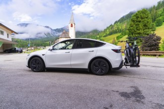 On a village road with a church in the background, a car in a mountain landscape, electric car on