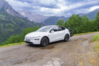 White car with bicycles on a winding mountain road, surrounded by dense greenery and cloudy sky,