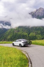 A car stands on a winding road with a view of misty mountains and green meadows, electric car on