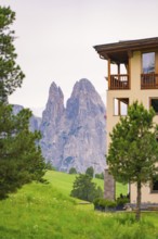 View of impressive rock formations behind a building with green foreground, Alpe di Siusi, South