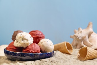 Different flavours of ice cream on a plate on the beach, with blue background and shell