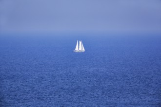 Blue sea, calm water surface, single sailing boat on the horizon, haze, offshore island Helgoland,