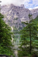An imposing mountain reflected in a clear mountain lake, framed by green trees and a slightly