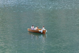 Three people in a small wooden boat on a quiet lake enjoying a relaxing trip, Lake Braies, South