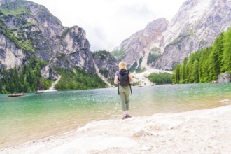 A woman enjoys the view from a lake shore of the majestic mountains all around, Pragser Wildsee,