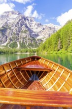 An empty wooden boat on a clear mountain lake with a view of steep rocks and wooded hills, Pragser