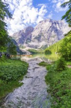 A clear mountain lake surrounded by impressive mountains and dense forest under a partly cloudy