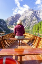 Back view of a woman in a boat on a mountain lake in sunny surroundings, Pragser Wildsee, South