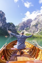 Man spreads his arms with joy on a boat on a mountain lake, Pragser Wildsee, South Tyrol,