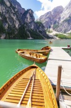 Several wooden boats are moored to a jetty on a calm, emerald-green mountain lake, Lake Braies,