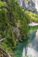 A narrow path winds along a steep slope with a view of an emerald green lake, Pragser Wildsee,