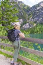 Person looking from a wooden fence at a mountain lake, surrounded by nature, Lake Braies, South