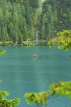A small red boat on a turquoise-blue lake, surrounded by dense forest, Pragser Wildsee, South