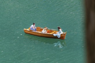 Three people in a wooden boat, floating relaxed on the water, in peaceful surroundings, Lake