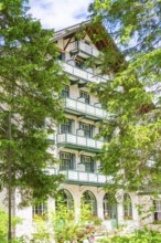 A white hotel building with balconies surrounded by green trees, Lake Braies, South Tyrol,