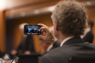 A person takes a photo with their mobile phone in front of the meeting of Federal Chancellor