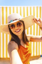 Fashionable tourist enjoying a sunny beach day, capturing joyful moments with a selfie while
