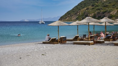 Kamari beach, Relaxed beach with sun loungers and parasols, Sailboat on the horizon in clear blue