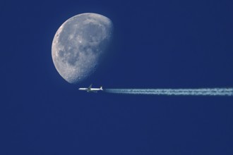 Aeroplane with contrails in front of a waning moon in the early morning sky, Bavaria, Germany