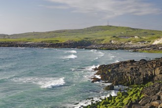 Rocky coastline with strong waves and green grassland under a cloudy sky, wild, Isle of Barra,