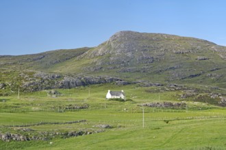 Small house in a green valley surrounded by mountains under clear skies, Isle of Barra, Hebrides,