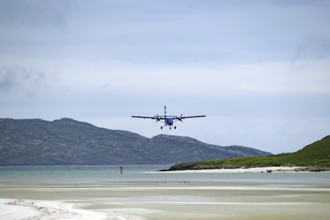 Small aeroplane approaching a beach surrounded by sea and mountains under a cloudy sky, Isle of