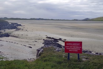 Empty beach with a warning sign in the foreground, surrounded by dunes and a wide sky, airport,