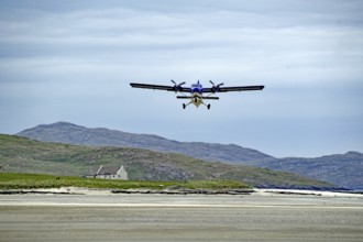 Low flying aeroplane over a runway in mountain landscape with cloudy sky, Isle of Barra, Hebrides,