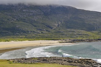 Expansive coastline with beach and waves against a mountain backdrop under a cloudy sky, Castlebay,