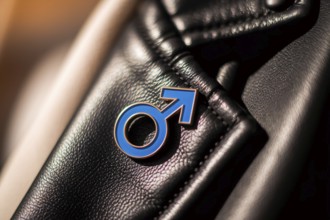Close-up of blue male gender symbol pin on worn black leather jacket symbolizing masculinity and