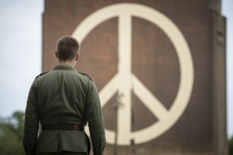 Back view of solitary soldier facing peace symbol on brick wall. Symbol of reflection, hope, and