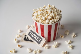 Red and white striped popcorn bucket with vintage movie tickets on white surface. Generative ai, AI
