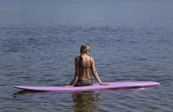 Woman, blonde, in bikini, sitting on board, surfboard, surfboard, purple, back, from behind,
