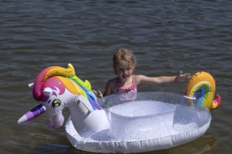 Girl, 3 years, blonde, playing with unicorn, swimming ring, inflatable, in the water, bathing lake,