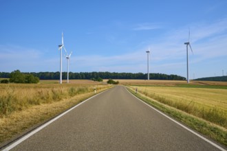 A road leads through fields, flanked by several wind turbines under a clear sky, summer, Wenkheim,