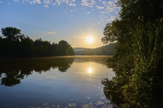 Sunbeams illuminate the calm river Main and the surrounding trees, the clear sky is gently
