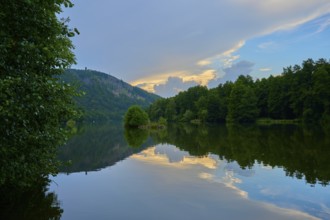 The calm river Main reflects trees and an impressive sky streaked with evening clouds, summer,