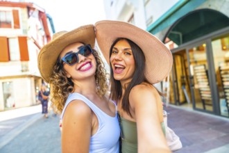 Two happy female tourists with straw hats and sunglasses taking a selfie while enjoying their