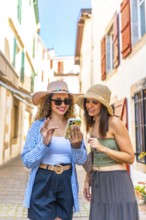 Two women are walking and using a smartphone in a typical small european street during a sunny day