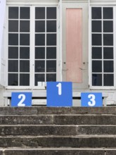 A winner's podium with the numbered places 1, 2 and 3, placed on a stone staircase in front of a