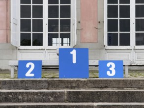 A winner's podium with the numbered places 1, 2 and 3, placed on a stone staircase in front of a