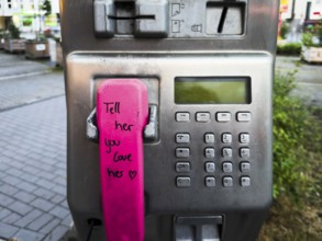 Telephone receiver of a Telekom payphone with the inscription Tell her you love her in Wuppertal,