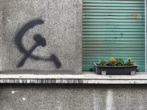 A hammer and sickle graffiti on a house wall next to a planted flower box in front of a roller