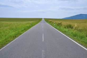A straight country road leads through wide fields to distant hills under a cloudy sky, Orferode,