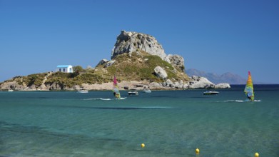 Island with windsurfers and boats in the turquoise blue sea in front of a rocky coast, Agios