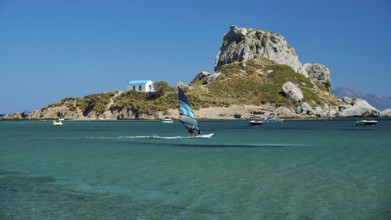 View of island with windsurfer and chapel in bright sunshine, Agios Stefanos Beach, Agios Stefanos