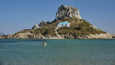 Small chapel with blue roof on rocky island in clear sea, Agios Stefanos Beach, Agios Stefanos