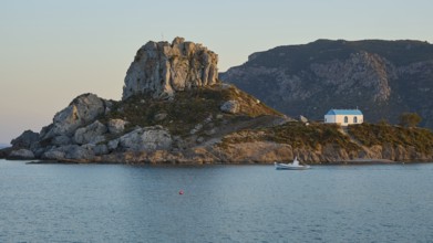 A small island with a chapel on a rock, surrounded by calm sea at sunrise, Agios Stefanos Beach,